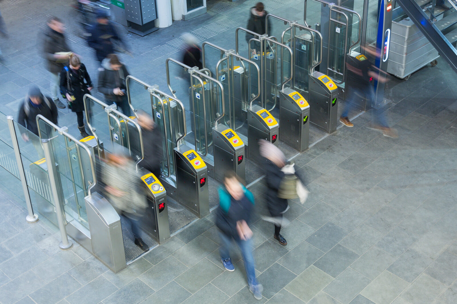 Reizigers lopen langs OV-poortjes in een stationshal en checken in met betaalpas of smartphone