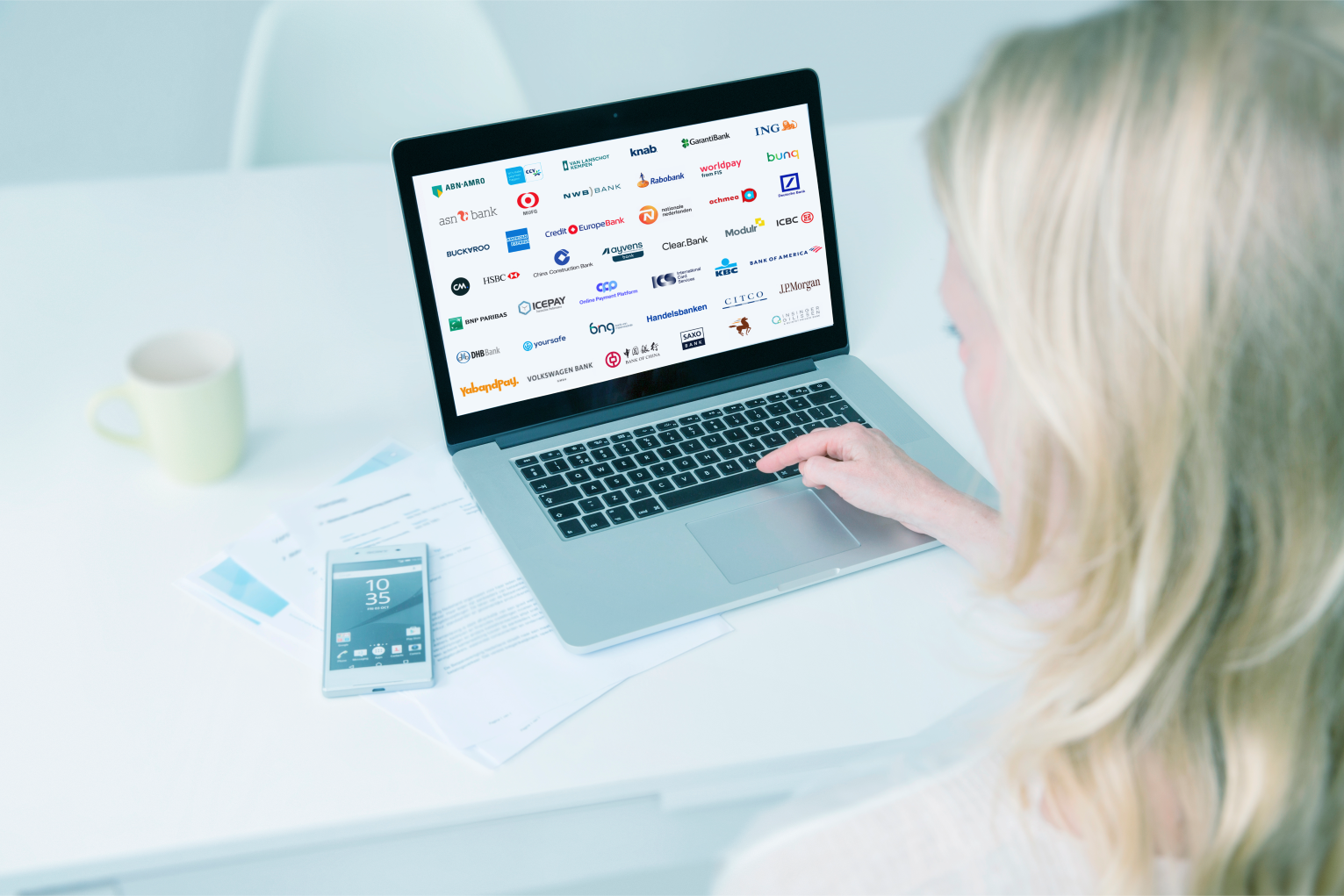 Vrouw kijkt naar laptopscherm met logos van leden van Betaalvereniging Nederland