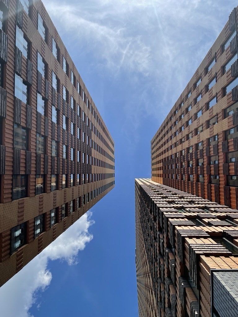 Foto genomen vanuit een laag standpunt tussen twee moderne bakstenen kantoorgebouwen met strakke lijnen, met daarboven een open blauwe lucht