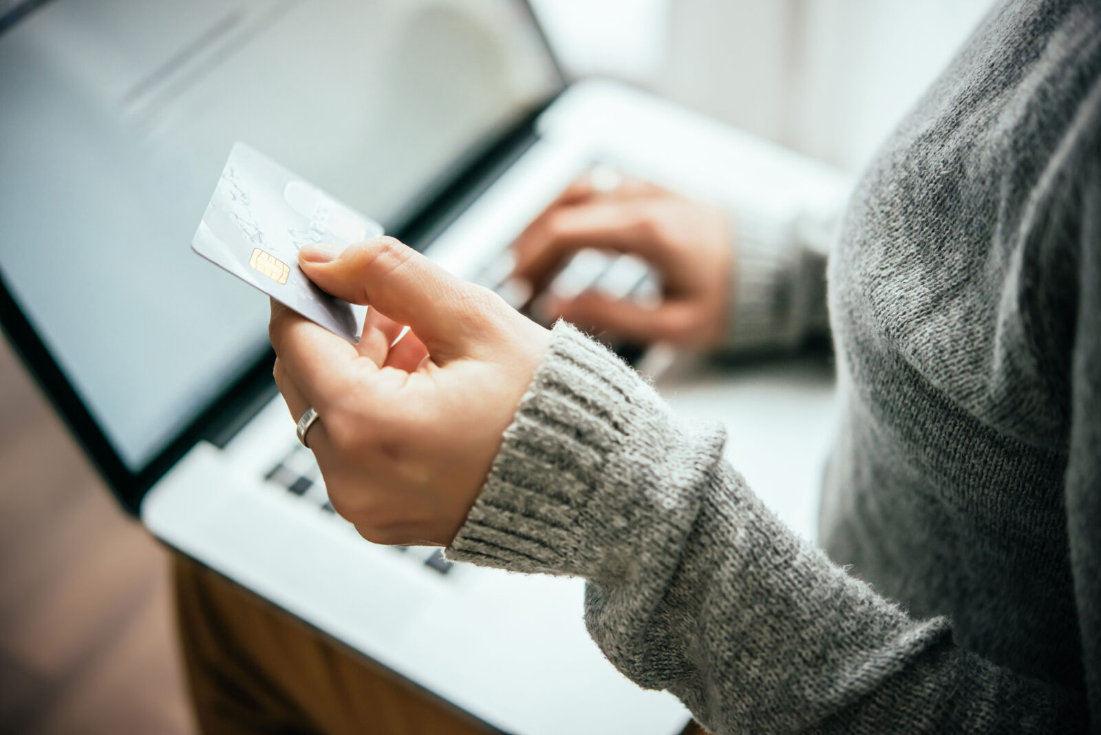 Persoon houdt een betaalpas vast terwijl online betaling wordt gedaan op een laptop in een rustige omgeving